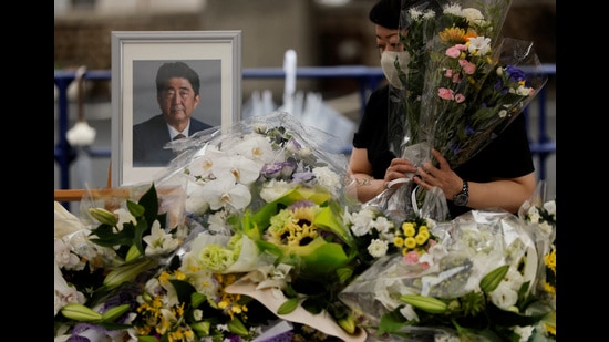 A mourner offers flowers next to a picture of late former Japanese Prime Minister Shinzo Abe, who was shot while campaigning for a parliamentary election, on the day to mark a week after his assassination at the Liberal Democratic Party headquarters, Tokyo, Japan July 15, 2022 (REUTERS)