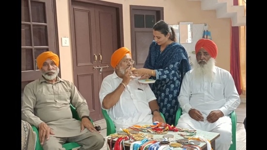 Gurdeep Singh’s father Bhag Singh (centre) and other family members celebrate with sweets as they watch the repeat telecast of his stellar performance, in Majri village in Khanna on Thursday. (HT Photo)