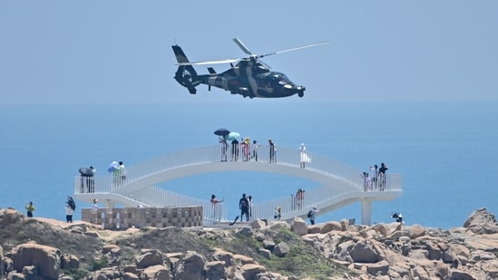 Tourists look on as a Chinese military helicopter flies past Pingtan island, one of mainland China's closest point from Taiwan, in Fujian province on August 4, 2022, ahead of massive military drills off Taiwan following US House Speaker Nancy Pelosi's visit to the self-ruled island. China is due on August 4 to kick off its largest-ever military exercises encircling Taiwan, in a show of force straddling vital international shipping lanes following a visit to the self-ruled island by US House Speaker Nancy Pelosi. &nbsp;(Photo by Hector RETAMAL / AFP)
