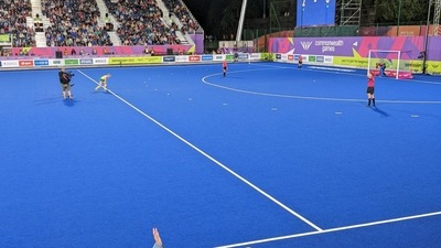 The technical delegate on the sidelines (in blue, left) has her hand held up with players in position.