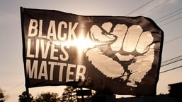 The setting sun shines through a Black Lives Matter flag
