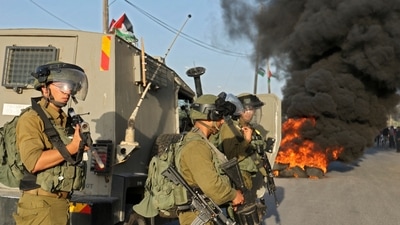 Israeli security forces take positions as Palestinians burn tyres during clashes after an attempt by Isreali settlers to remove Palestinian flags east of the West Bank village of Qalqiliya, on May 31, 2022. (AFP) Israeli security forces take positions as Palestinians burn tyres during clashes after an attempt by Isreali settlers to remove Palestinian flags east of the West Bank village of Qalqiliya, on May 31, 2022. (AFP)