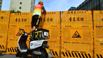 A courier stands on an electric bike to make a delivery over a barricade, amid lockdown measures to curb the coronavirus disease (Covid-19) outbreak in Sanya, Hainan province, China. (REUTERS) A courier stands on an electric bike to make a delivery over a barricade, amid lockdown measures to curb the coronavirus disease (Covid-19) outbreak in Sanya, Hainan province, China. (REUTERS)