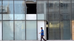Uma foto tirada em 12 de agosto de 2022 mostra vidro quebrado enquanto um homem caminha em frente ao prédio onde, de acordo com autoridades sauditas, um suspeito de um ataque mortal do grupo Estado Islâmico em 2015 a uma mesquita saudita se explodiu enquanto era preso pela segurança forças em Jeddah esta semana.
