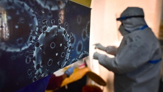 An illustration of the novel coronavirus seen next to a health care worker at a Covid-19 testing centre in New Delhi.