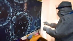An illustration of the novel coronavirus seen next to a health care worker at a Covid-19 testing centre in New Delhi.