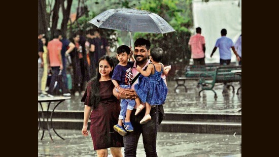 A couple shielding their children with an umbrella amid rain at Sukhna Lake on Sunday. The showers caused the mercury to drop by four degrees between 5.30 pm and 8.30 pm. (Keshav Singh/HT)