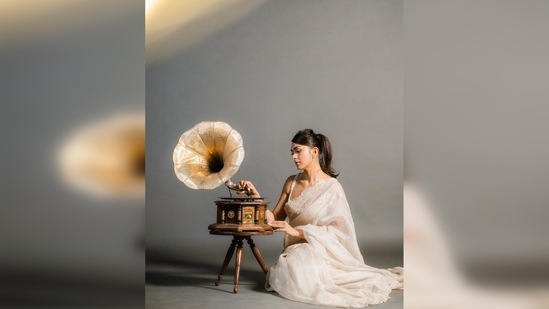 To add more vintage charm to her shoot, Mrunal Thakur posed with a gramophone in front of a plain backdrop.(Instagram/@mrunalthakur)