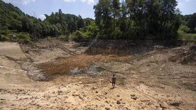 Gan Bingdong walks through the basin of a community reservoir near his farm that ran nearly empty after its retaining wall started to leak and hot weather and drought conditions accelerated the loss of water, in Longquan village in southwestern China's Chongqing Municipality, on Saturday. (AP) Gan Bingdong walks through the basin of a community reservoir near his farm that ran nearly empty after its retaining wall started to leak and hot weather and drought conditions accelerated the loss of water, in Longquan village in southwestern China's Chongqing Municipality, on Saturday. (AP)