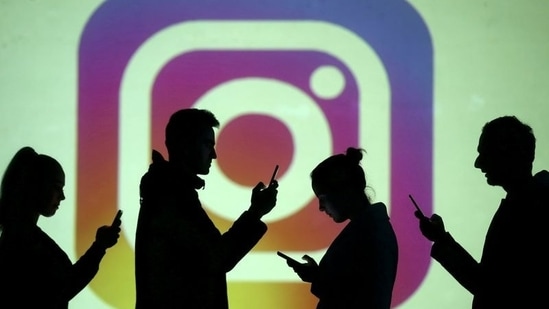Silhouettes of mobile users are seen next to a screen projection of Instagram logo in this picture illustration.(REUTERS)