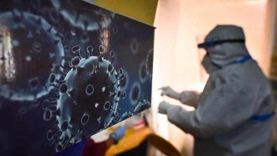 An illustration of the novel coronavirus seen next to a health care worker at a Covid-19 testing centre in New Delhi. (Sanchit Khanna / HT Photo)