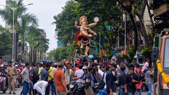 Devotees walk alongside an idol of elephant-headed Hindu deity Ganesha through a street, ahead of the Ganesh Chaturthi festival in Mumbai.(AFP)