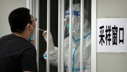 Un trabajador que usa un traje protector toma una muestra de la garganta de un hombre para una prueba de Covid-19 en un sitio de prueba de coronavirus en Beijing.