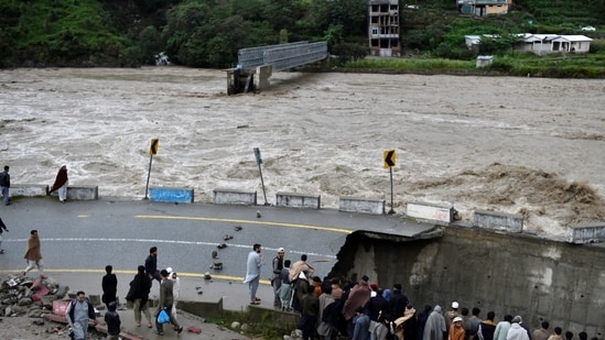 People gather next to a section of a road damaged by flood waters following heavy monsoon rains in Madian area in Pakistan's northern Swat Valley.(AFP)