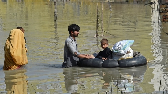 Uma família atravessa uma área inundada após fortes chuvas de monção no distrito de Charsadda, em Khyber Pakhtunkhwa. (AFP)