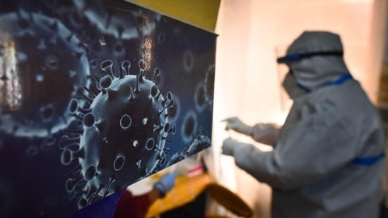 An illustration of the novel coronavirus seen next to a health care worker at a Covid-19 testing centre. (Sanchit Khanna / HT Photo)