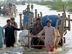 TOPSHOT - Stranded people along with their belongings wade through a flooded street after fleeing from their flood hit homes following heavy monsoon rains at Sohbatpur area in Jaffarabad district of Balochistan province.&nbsp;(AFP)
