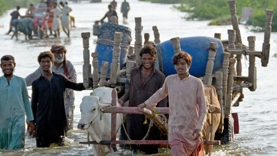 TOPSHOT - Stranded people along with their belongings wade through a flooded street after fleeing from their flood hit homes following heavy monsoon rains at Sohbatpur area in Jaffarabad district of Balochistan province.&nbsp; (AFP)