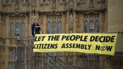 A Extinction Rebellion protester sits next to a banner outside the Palace of Westminster, where inside the House of Commons, ER protesters have glued themselves to the Speakers Chair in London, Friday,&nbsp; (AP)