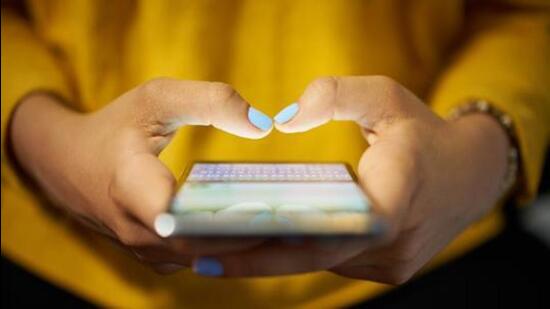 Young woman using cell phone to send text message on social network at night. Closeup of hands with computer laptop in background (Getty Images/iStockphoto)