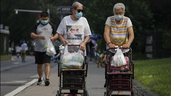 Elderly women push their wheelchairs loaded with groceries as they walk along a street in Beijing, China. (AP)