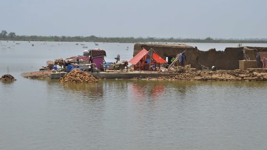 A family sit under a tent in their damaged home surrounded by flood, in Jaffarabad, a district of Pakistan.(AP)