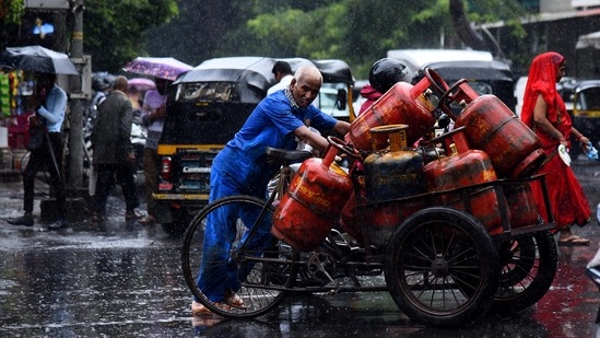 A worker trudges with his tricyle loaded with cooking gas cylinders for delivering to customers in the rain.