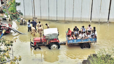 People commute in a tractor trolley as firemen stand next to pumps that are used to remove water from a water-logged neighbourhood following torrential rains in Bengaluru. (REUTERS)