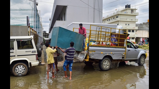 Residents carrying their belongings shift from a flooded locality of Bellandur after heavy monsoon rains, in Bengaluru. (PTI)