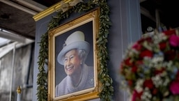 Um retrato da rainha Elizabeth II da Grã-Bretanha está pendurado ao lado de tributos florais do lado de fora de um shopping center.