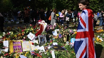 Queen Elizabeth II's Funeral: A young girl wearing a Union Jack flag looks at floral tributes placed by members of the public in remembrance of Britain's Queen Elizabeth II. (AFP)