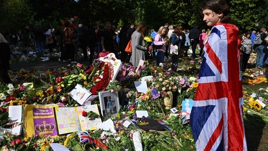 Queen Elizabeth II's Funeral: A young girl wearing a Union Jack flag looks at floral tributes placed by members of the public in remembrance of Britain's Queen Elizabeth II.(AFP)