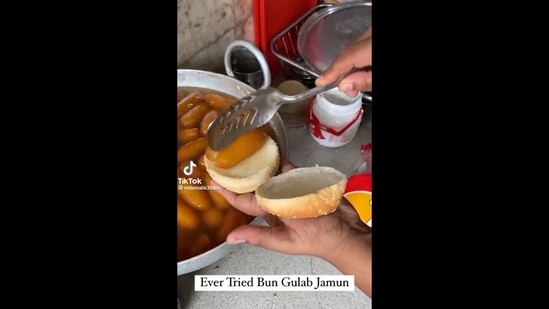 The image, taken from the video re-posted on Twitter, shows an individual slicing gulab jamun in half on the bun to make a gulab jamun burger. The text insert reads, “Ever tried bun gulab jamun.”(Twitter/@Tabeshq)