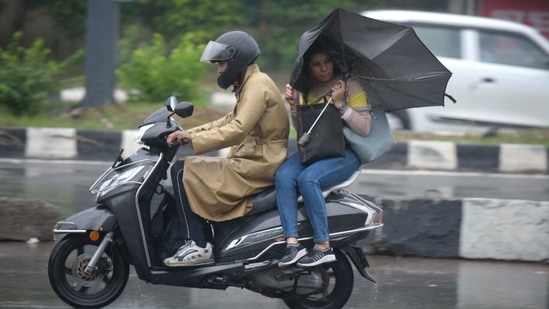 Commuters on a two-wheeler could be seen attempting to shield themselves from the rain in Gurugram. (Photo by Parveen Kumar/Hindustan Times)