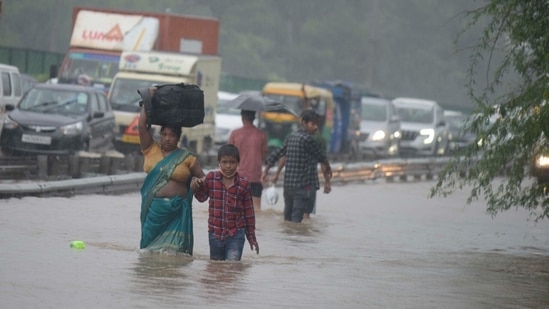 A woman tries to cross an inundated service road in Gurugram while carrying baggage on her head and holding a child's hands. (Photo by Parveen Kumar/Hindustan Times)