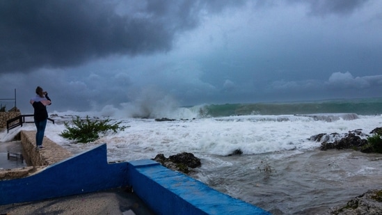 A woman takes photos while waves crash against a seawall as Hurricane Ian passes through George Town, Grand Cayman island.(AP)