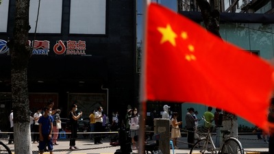 China: A China's flag flutters near people lining up to get tested at a makeshift nucleic acid testing site.&nbsp; (Reuters)
