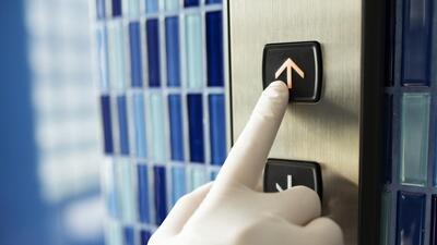 Gloved hand pressing an elevator button to prevent coronavirus contamination (rawpixel.com / roungroat)