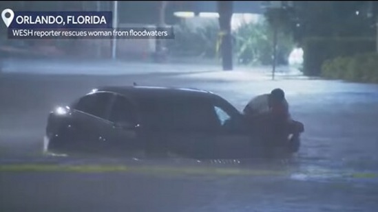 The image, taken from the Instagram video, shows the reporter rescuing a woman stranded in floodwaters in Orlando.(Instagram/@wesh2)