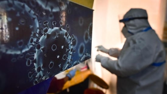 Covid Cases In India: An illustration of the novel coronavirus seen next to a health care worker at a Covid-19 testing centre in New Delhi.(HT Photo)