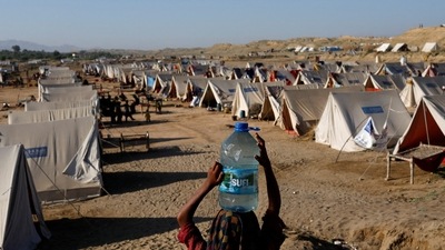 Pakistan Floods: A displaced girl carries a bottle of water she filled from nearby stranded flood-waters, as her family takes refuge in a camp, in Sehwan, Pakistan. (Reuters)