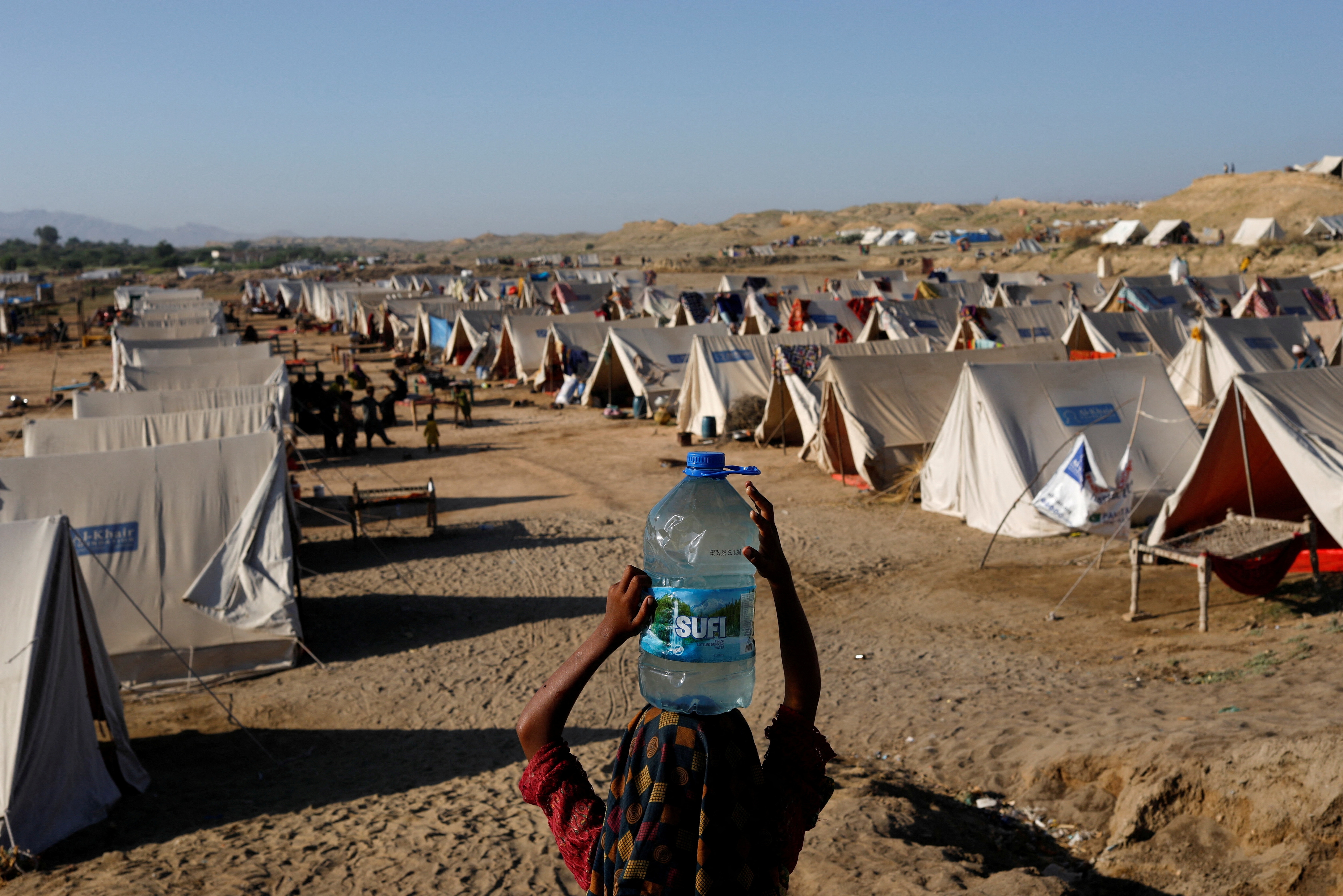 Pakistan Floods: A displaced girl carries a bottle of water she filled from nearby stranded flood-waters, as her family takes refuge in a camp, in Sehwan, Pakistan. (Reuters)