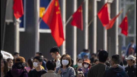 People wearing face masks walk near Chinese flags hung along a pedestrian shopping street in Beijing. (AP) People wearing face masks walk near Chinese flags hung along a pedestrian shopping street in Beijing. (AP)