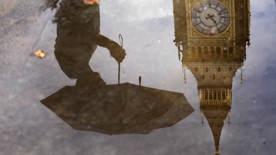 Britain Power Cuts: A woman with an umbrella and the Elizabeth Tower also known as Big Ben are reflected in a puddle in London.(AP)