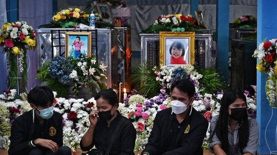 Relatives sit in front of the coffins of victims of the nursery mass shooting at Wat Si Uthai temple in Thailand's northeastern Nong Bua Lam Phu province on October 8, 2022. (Photo by Lillian SUWANRUMPHA/AFP)