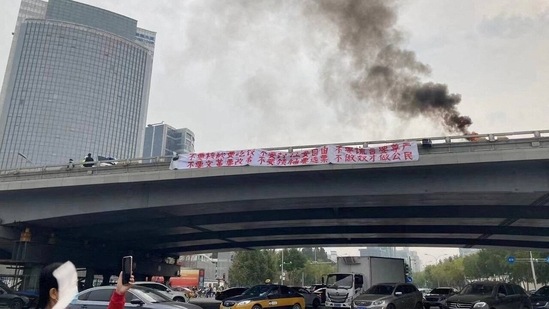 China Protests: Smoke rises as a banner with a protest message hangs off Sitong Bridge, Beijing, China.(Reuters)
