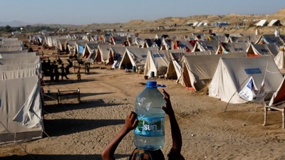 Pakistan Floods: A displaced girl carries a bottle of water she filled from nearby stranded flood-waters, as her family takes refuge in a camp, in Sehwan, Pakistan. (Reuters)