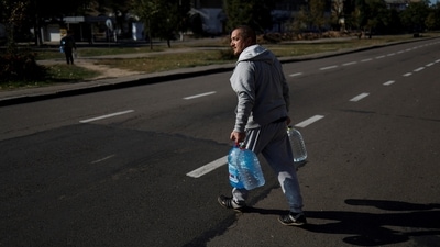Russia-Ukraine War: A local man crosses a street with filled bottles of fresh drinking water in Kherson region. (Reuters)