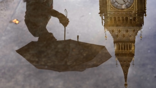 UK Cost Of Living Crisis: A woman with an umbrella and the Elizabeth Tower also known as Big Ben are reflected in a puddle in London.(AP)