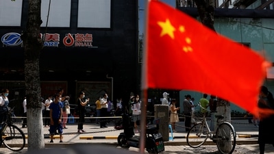 A China's flag flutters near people lining up to get tested at a makeshift nucleic acid testing site.&nbsp; (Reuters)